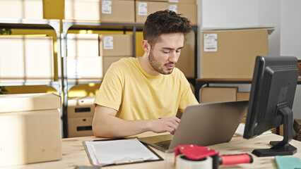 Young hispanic man ecommerce business worker using laptop with serious face at office