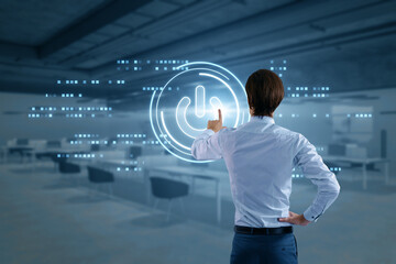 Back view of man hand using glowing digital power button on blurry office interior background....