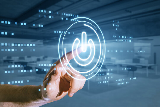 Close up of hand using glowing digital power button on blurry office interior background. Computer and technology concept.