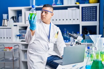 Young latin man scientist holding test tube using laptop at laboratory