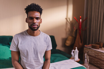 Homem negro sentado na cama com expressao seria.