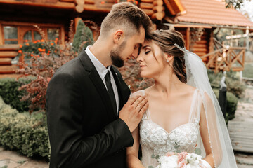 gorgeous elegant luxurious bride with veil blowing in the wind. and a stylish groom kiss outdoors near tall autumn trees