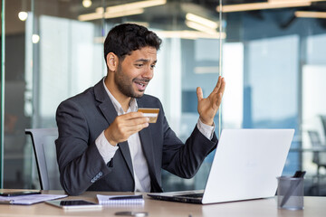 Cheated and unsatisfied disappointed businessman with bank credit card and laptop inside office, man received error, and rejected online money transfer at workplace.