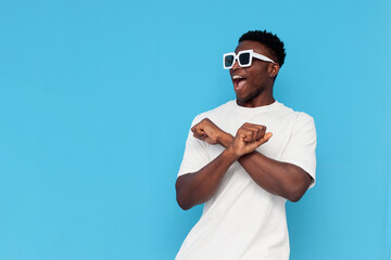 african american man in white t-shirt and sunglasses dances to music and sings on blue isolated background