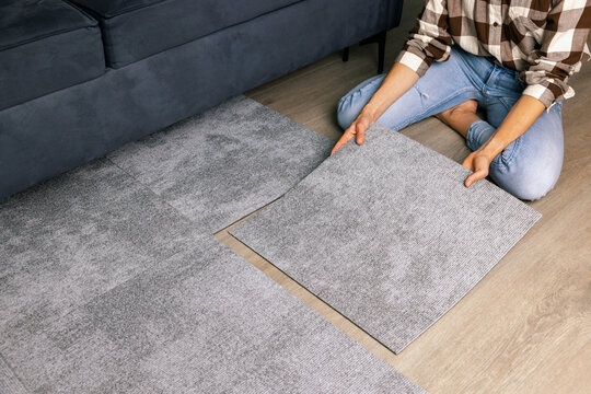 woman laying carpet tiles on floor in living room at home
