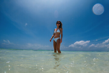 Portrait of a beautiful slim woman standing in sea water on beach in bikini.