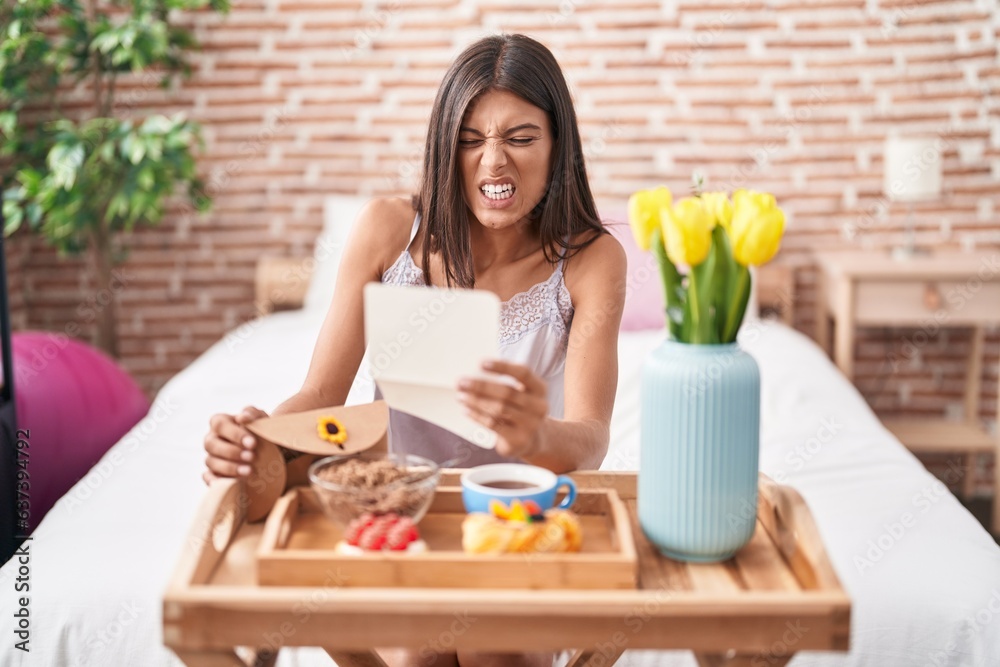 Poster Brunette young woman eating breakfast in the bed reading a letter angry and mad screaming frustrated and furious, shouting with anger looking up.