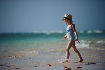 Portrait of a beautiful little girl walking on the beach in a swimsuit and a straw hat.
