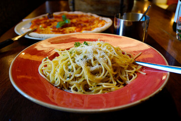 a large red plate of delicious, hot spaghetti aglio e olio sprinkled with Parmigiano at a...
