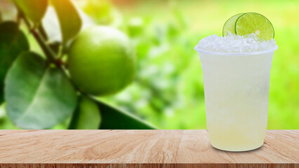 Cool freshly made lemonade in a plastic cups with crushed ice and lemon slices on wooden table with green limes raw lemon hanging on lemon tree background