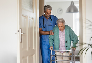 Caregiver helping senior woman to walk in her home with walker.