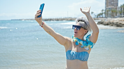 Young woman tourist wearing bikini and hawaiian lei having video call at beach