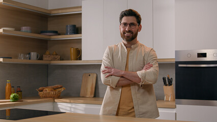 Moving shot adult Caucasian man in glasses at home modern kitchen posing hands crossed smiling to...
