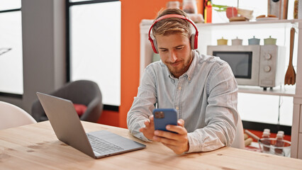 Young caucasian man listening to music sitting on table at dinning room