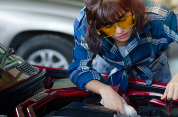 Asian woman auto mechanic work in vehicle repair shop, check and repair under body and suspension system, holding mechanic's work lamp, international Women's day