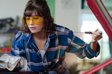 Asian woman auto mechanic work in vehicle repair shop, check for lubricant depletion, international Women's day