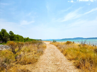 Rocky road leading to beautiful beach at the end of the road. Sunny summer walk by the blue sea 