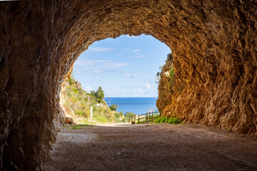 At the entrance of the Zingaro National Park you have a view from a rock tunnel with gravel ends to the blue sea and the blue sky.