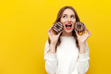 young cute girl holding two chocolate donuts over yellow isolated background, woman screaming with...