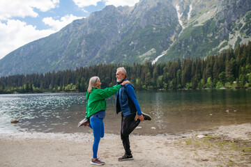 Senior couple doing outdoor yoga by the lake in the mountains.