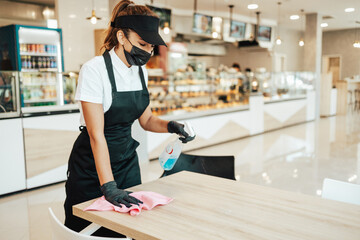 Beautiful woman working bakery or fast food restaurant. She is cleaning and disinfecting tables...