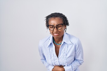 African woman with dreadlocks standing over white background wearing glasses with hand on stomach because nausea, painful disease feeling unwell. ache concept.