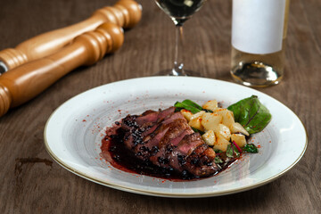 Sliced duck breast with potatoes and wine on wooden table