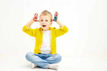 a little boy child with painted hands stained in paint in yellow clothes on a white isolated background was drawing