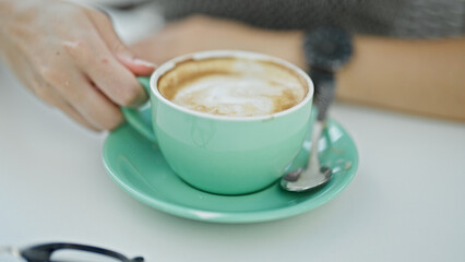 Young blonde woman holding cup of coffee at coffee shop terrace
