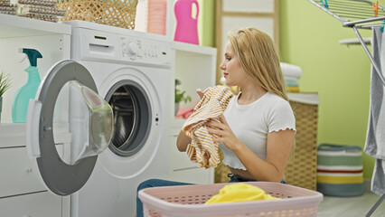 Young blonde woman smiling confident washing clothes at laundry room