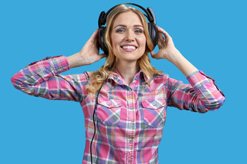 Attractive young blond woman wearing headphones and holding it with both hands. Isolated on vivid blue background.