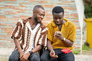 image of african guys with smartphone outside- two black guys wearing woven dress enjoying social...