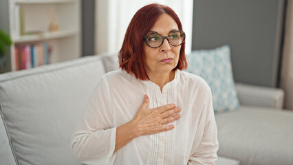 Middle age woman sitting on sofa suffering chest pain at home