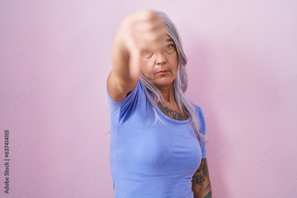 Sticker middle age woman with tattoos standing over pink background looking unhappy and angry showing reject