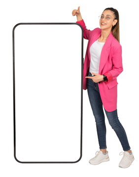 Big mobile phone mock up,  full body young smiling caucasian business woman in pink jacket stand near big mobile phone mock up. Point finger smartphone empty blank screen. Transparent, png background.