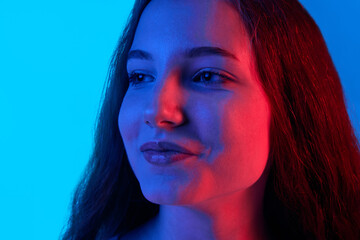 Calmness. Close-up of beautiful girl with little smile looking away against blue studio background in neon light. Concept of human emotions, fashion, youth, beauty, lifestyle, ad