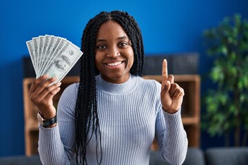 African american woman holding dollars banknotes smiling with an idea or question pointing finger...