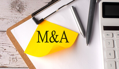 M and A word on yellow sticky with calculator, pen and clipboard