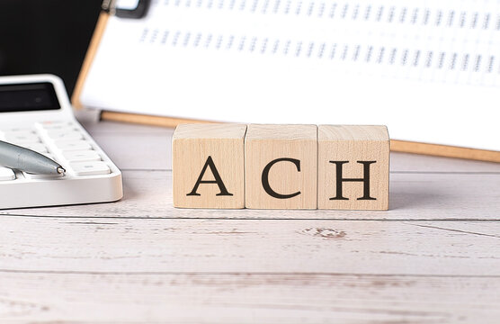 ACH Automated Clearing House word on a wooden block with clipboard and calcuator