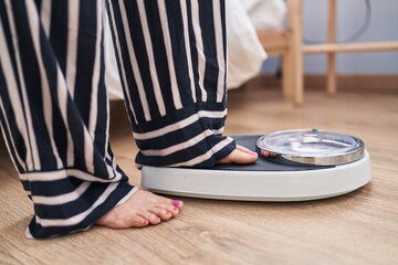 Young caucasian woman using weighing machine at bedroom
