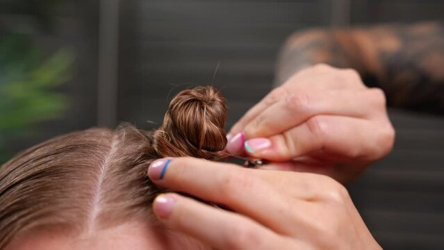 Professional hairdresser making small space bun on girl client wet hair. Hair styling with hairpins and black comb. Professional beauty salon