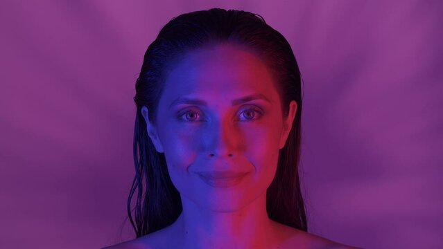 Close up video of a young woman's face. She's confidently looking at the camera as the feather is uncovering her eyes, neon solor scheme. HDR BT2020 HLG Material.