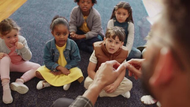 First grade teacher teaching a group of young children the alphabet song, actively engaging in the lesson using his fingers. Male elementary school educator leading his class in a nursery rhyme.