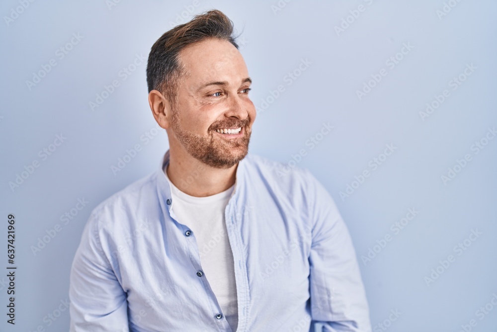 Sticker middle age caucasian man standing over blue background looking away to side with smile on face, natu