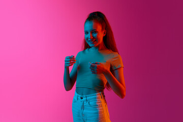 Portrait of beautiful young girl smiling against pink studio background in neon light. Happiness. Concept of human emotions, fashion, beauty, lifestyle, youth, ad