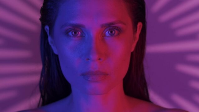 Close up video of a young woman's face. She's confidently looking at the camera as the feather is uncovering her eyes, neon solor scheme. HDR BT2020 HLG Material.
