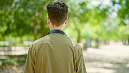 Young hispanic man standing backwards wearing headphones at park