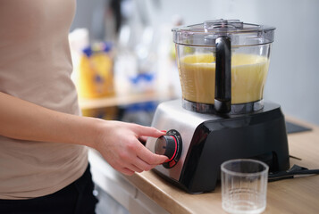 Fototapeta na wymiar Woman is making smoothie or mixing dough in electric blender. Blender and food mixer concept