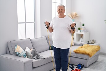 Middle age grey-haired man smiling confident using elastic band training at home
