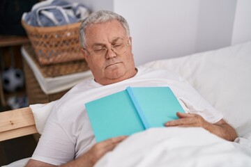 Middle age grey-haired man lying on bed sleeping holding book at bedroom